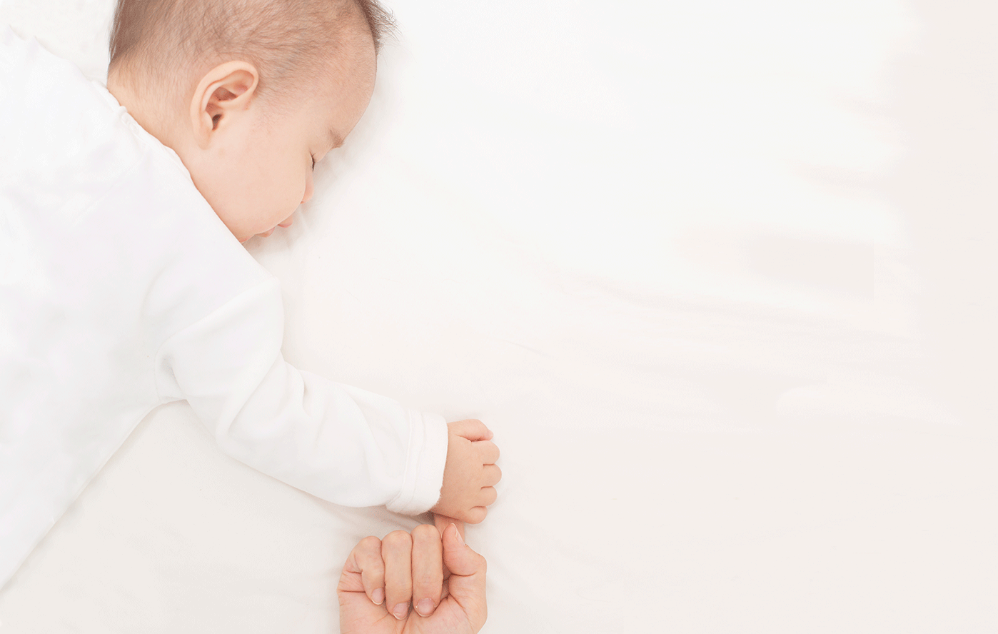 母親の指を握って眠る赤ちゃん